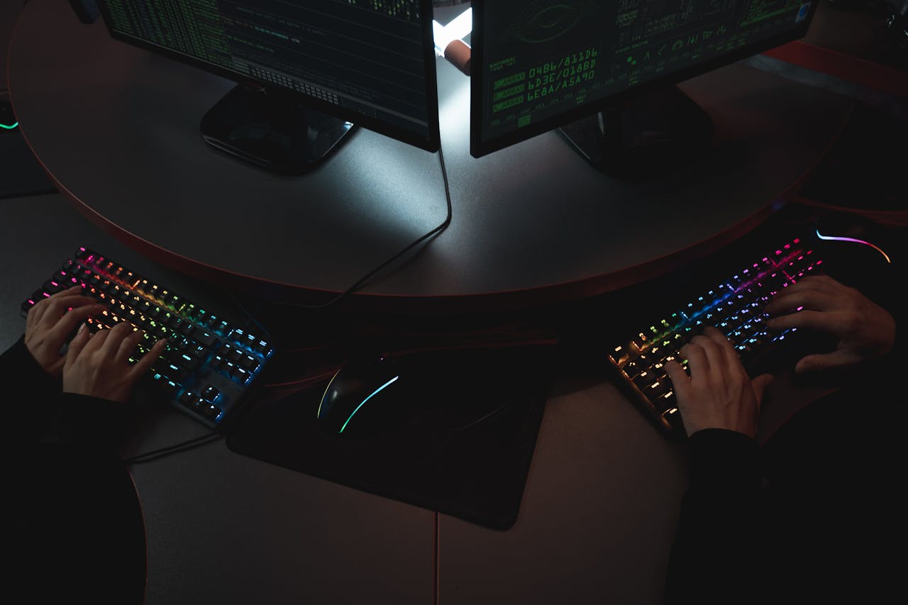 Two people typing on RGB keyboards with code on screens, indicating a cybersecurity environment.